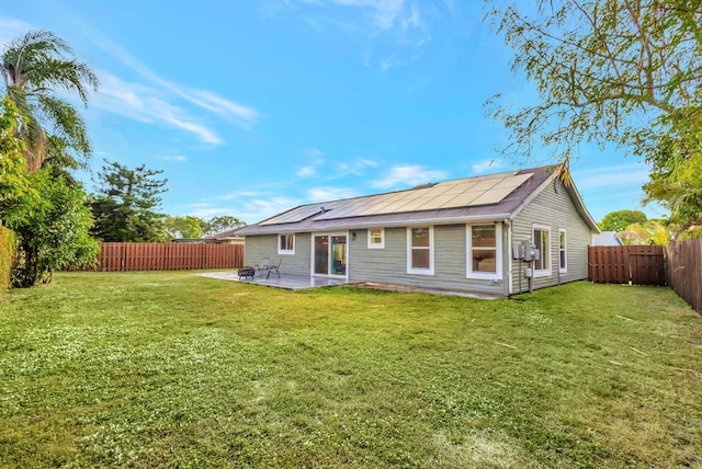 back of house featuring a lawn, a patio area, and solar panels