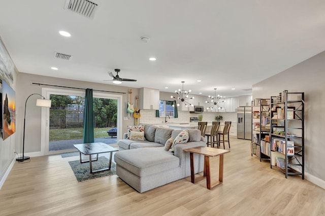 living room featuring sink, ceiling fan with notable chandelier, and light wood-type flooring