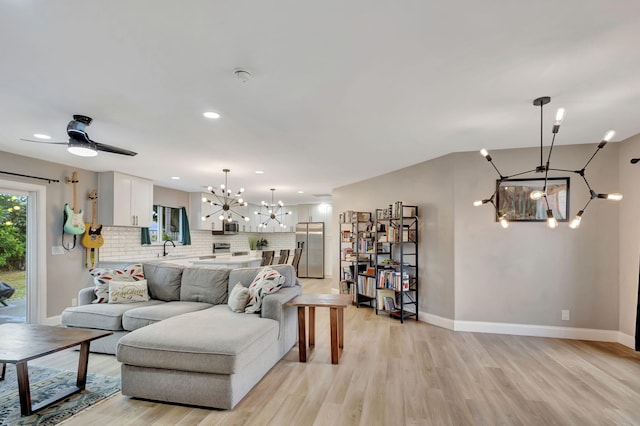 living room featuring ceiling fan with notable chandelier and light hardwood / wood-style flooring