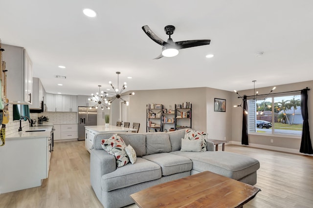 living room featuring light hardwood / wood-style flooring, ceiling fan with notable chandelier, and sink