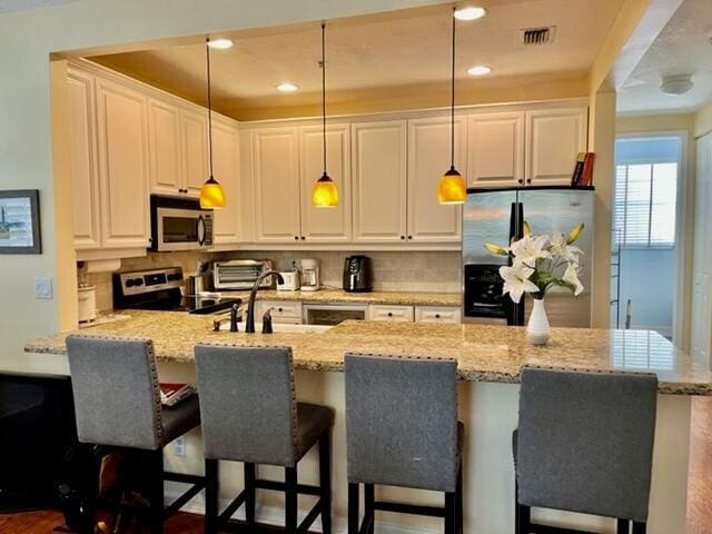 kitchen featuring white cabinets, appliances with stainless steel finishes, and decorative light fixtures