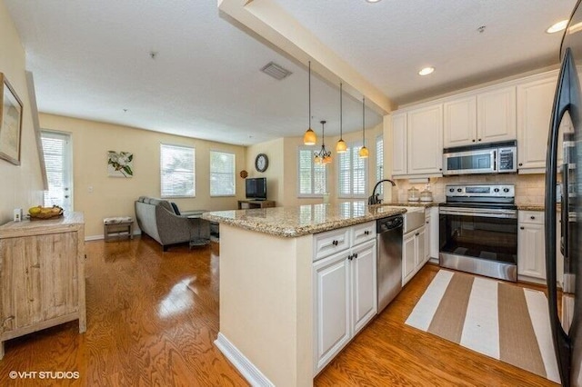 kitchen with backsplash, kitchen peninsula, hardwood / wood-style floors, pendant lighting, and appliances with stainless steel finishes