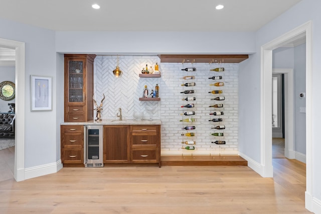 bar with beverage cooler, tasteful backsplash, sink, hanging light fixtures, and light wood-type flooring