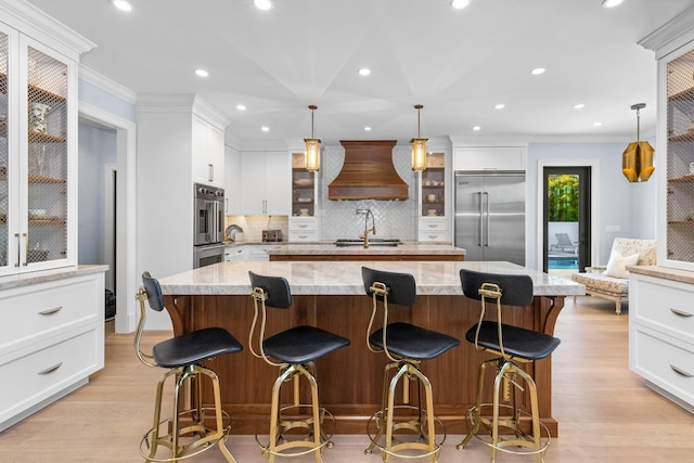 kitchen with custom exhaust hood, stainless steel appliances, decorative light fixtures, and a large island