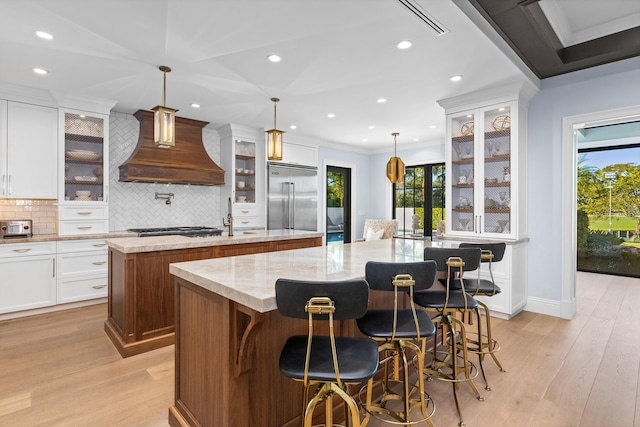 kitchen featuring custom range hood, decorative light fixtures, a large island, appliances with stainless steel finishes, and a breakfast bar