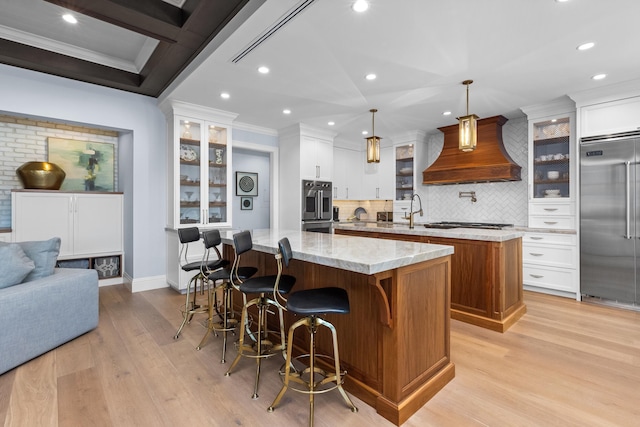 kitchen featuring a large island, decorative light fixtures, custom exhaust hood, appliances with stainless steel finishes, and light stone counters