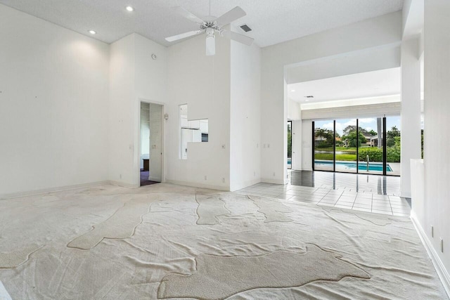 spare room with light carpet, a towering ceiling, a textured ceiling, and ceiling fan