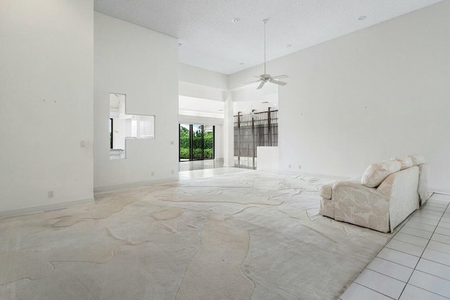 unfurnished living room featuring ceiling fan, a towering ceiling, and a textured ceiling