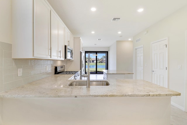 kitchen featuring white cabinetry, light stone countertops, backsplash, light tile patterned floors, and appliances with stainless steel finishes