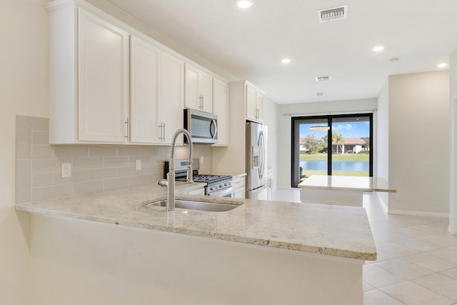 kitchen featuring kitchen peninsula, white cabinetry, light stone counters, and appliances with stainless steel finishes