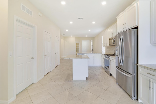 kitchen with white cabinetry, a center island, light stone counters, light tile patterned floors, and appliances with stainless steel finishes