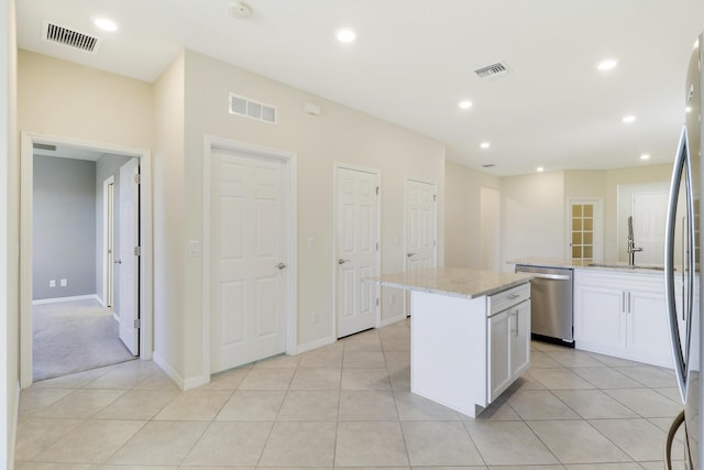 kitchen featuring light stone countertops, dishwasher, a kitchen island, light tile patterned flooring, and white cabinets