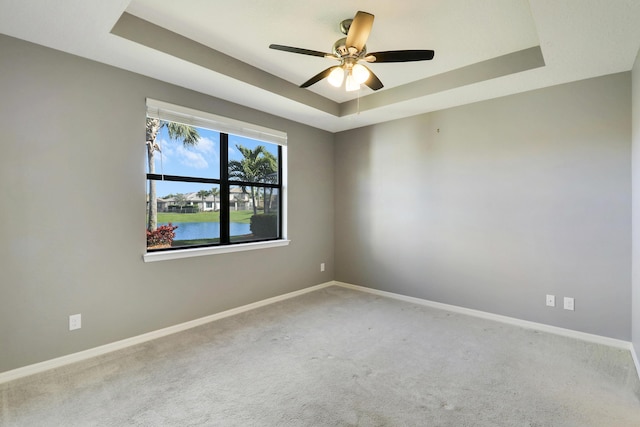 spare room featuring a tray ceiling, ceiling fan, and a water view