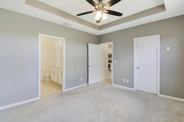 unfurnished bedroom with a raised ceiling, ensuite bath, ceiling fan, and light colored carpet