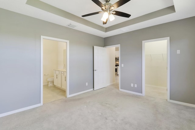 unfurnished bedroom featuring a raised ceiling, a walk in closet, ceiling fan, and connected bathroom