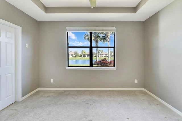 empty room with a raised ceiling, a water view, and light colored carpet