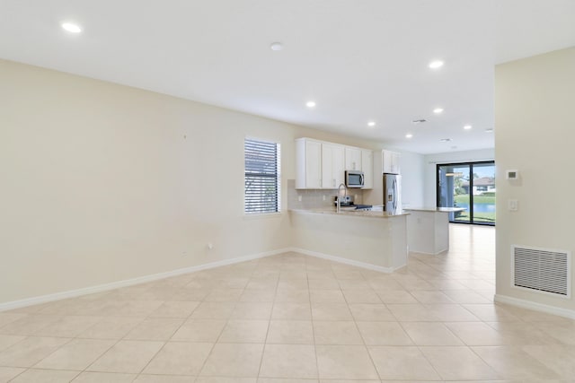 kitchen with a kitchen breakfast bar, kitchen peninsula, light tile patterned floors, appliances with stainless steel finishes, and white cabinetry