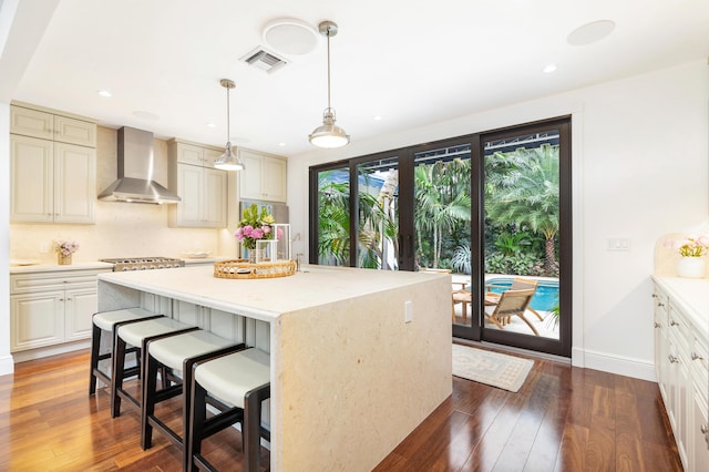 kitchen with a center island, wall chimney range hood, dark hardwood / wood-style flooring, and decorative light fixtures