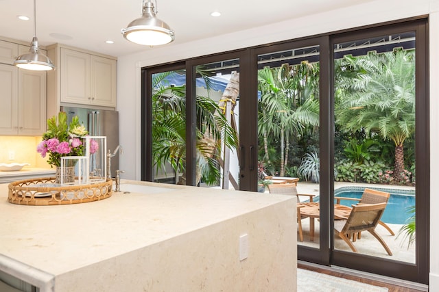 kitchen featuring cream cabinets, decorative light fixtures, sink, high end refrigerator, and light stone countertops