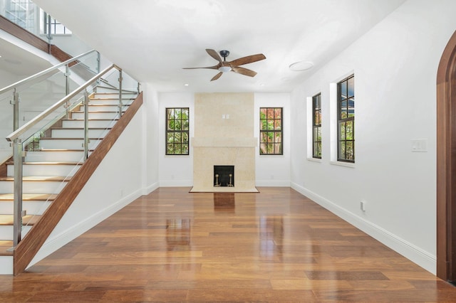 unfurnished living room with ceiling fan, plenty of natural light, a fireplace, and wood-type flooring