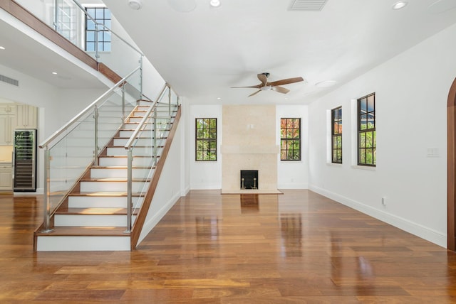 unfurnished living room with hardwood / wood-style flooring, beverage cooler, a premium fireplace, and ceiling fan