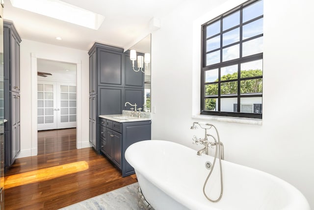 bathroom with a skylight, wood-type flooring, vanity, a washtub, and french doors