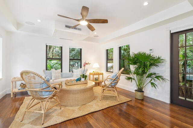 living room with ceiling fan, a tray ceiling, and dark hardwood / wood-style floors