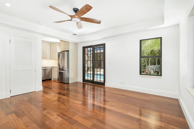 unfurnished room with ceiling fan, plenty of natural light, a tray ceiling, and wood-type flooring