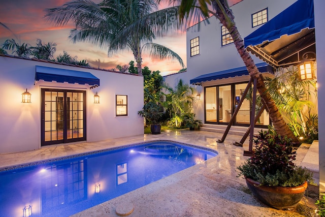 pool at dusk featuring french doors and a patio area