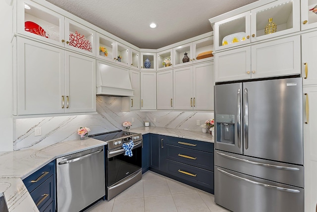 kitchen with light tile patterned floors, tasteful backsplash, custom range hood, appliances with stainless steel finishes, and blue cabinets