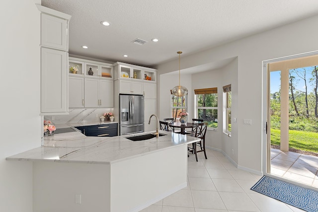 kitchen featuring kitchen peninsula, sink, white cabinets, stainless steel fridge with ice dispenser, and hanging light fixtures