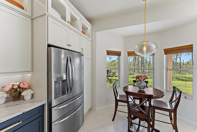 kitchen with light stone countertops, white cabinets, stainless steel fridge with ice dispenser, pendant lighting, and light tile patterned flooring