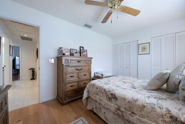 bedroom featuring a textured ceiling, light hardwood / wood-style floors, ceiling fan, and multiple closets