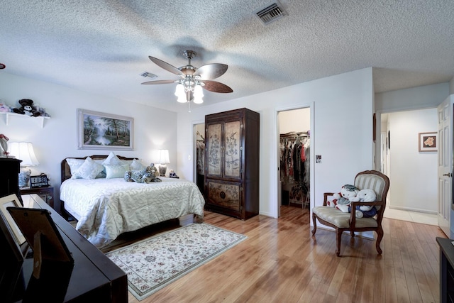 bedroom featuring ceiling fan, light hardwood / wood-style flooring, a textured ceiling, a walk in closet, and a closet