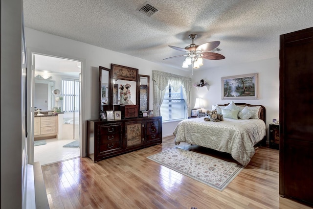 bedroom featuring ensuite bath, ceiling fan, light hardwood / wood-style floors, and a textured ceiling