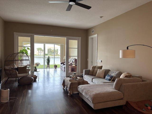 living room with a textured ceiling, dark wood-type flooring, ceiling fan, and a water view