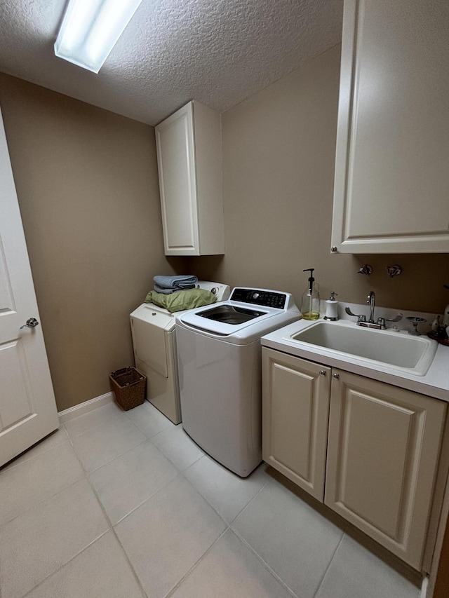 clothes washing area featuring sink, light tile patterned floors, washer and clothes dryer, cabinets, and a textured ceiling