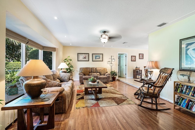 living room with ceiling fan, a textured ceiling, and light wood-type flooring