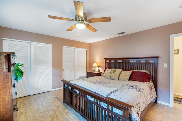 bedroom featuring ceiling fan, light hardwood / wood-style flooring, and two closets