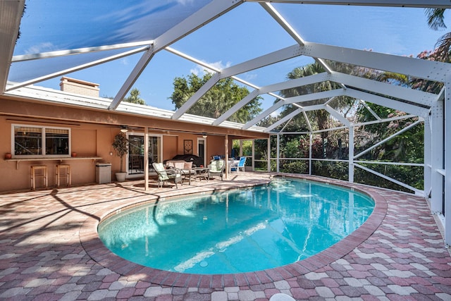 view of swimming pool featuring a patio, glass enclosure, and a bar