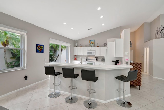 kitchen with a kitchen bar, white appliances, vaulted ceiling, and plenty of natural light