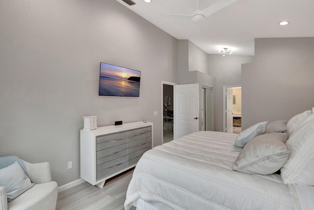 bedroom with a high ceiling, connected bathroom, light hardwood / wood-style floors, and ceiling fan