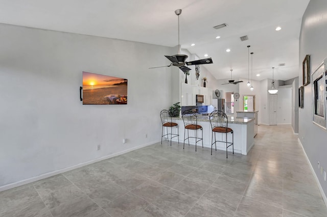 kitchen featuring light stone countertops, a breakfast bar, ceiling fan, decorative light fixtures, and white cabinetry