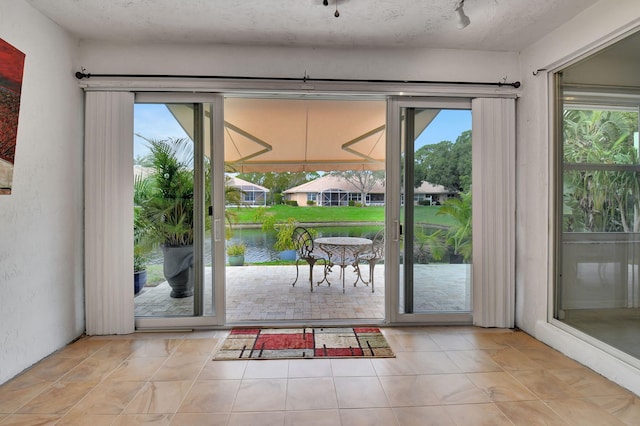 doorway to outside with a water view, light tile patterned flooring, and a textured ceiling