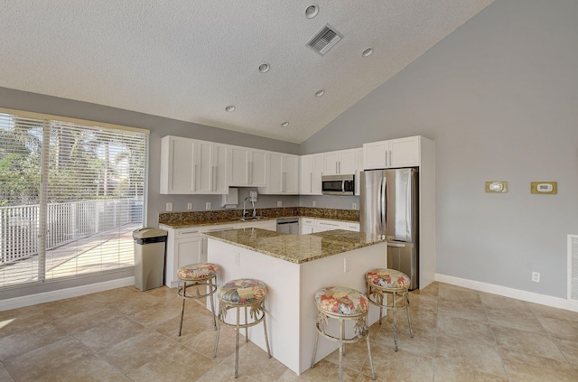 kitchen featuring a breakfast bar, stainless steel appliances, sink, dark stone countertops, and a center island