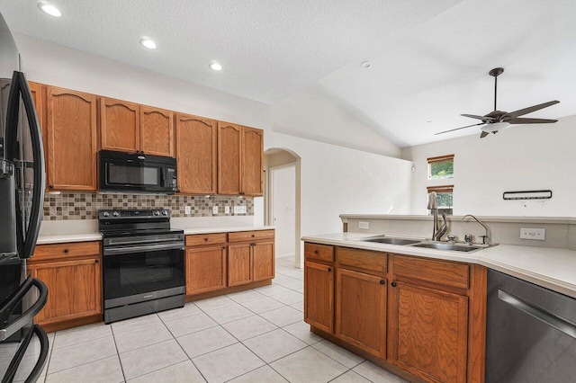 kitchen with decorative backsplash, vaulted ceiling, sink, black appliances, and light tile patterned floors