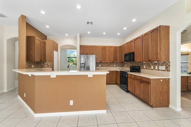 kitchen featuring decorative backsplash, a breakfast bar, light tile patterned floors, and black appliances