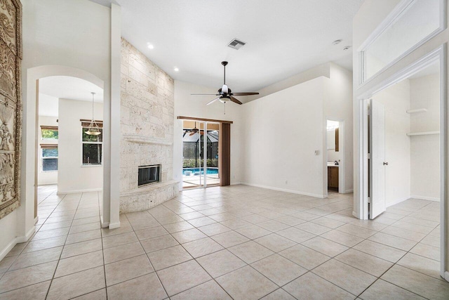 unfurnished living room featuring a stone fireplace, ceiling fan, a towering ceiling, and light tile patterned flooring