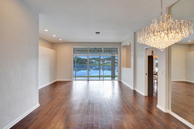 unfurnished room with a textured ceiling, dark hardwood / wood-style floors, a notable chandelier, and a water view