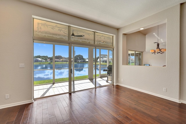 empty room featuring ceiling fan with notable chandelier, a water view, and dark wood-type flooring